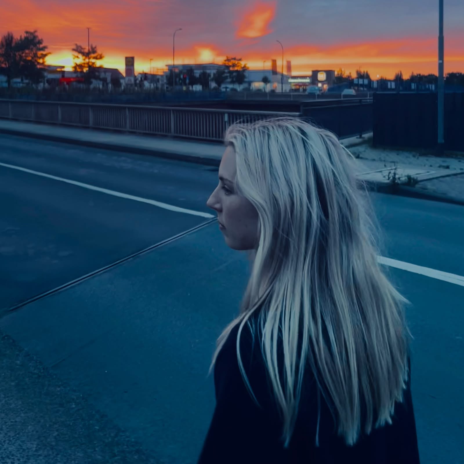 ghoulgirl in profile beside a road under an orange and blue sunset
